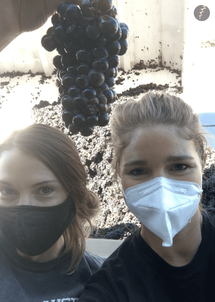 Lisa and her friend wearing face masks holding up a bunch of grapes