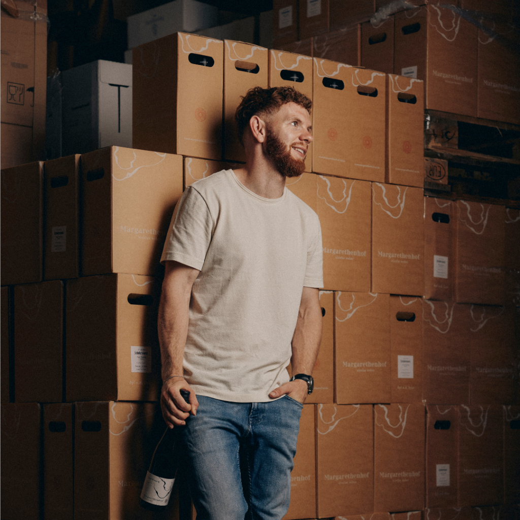 Nicoals Weber in front of wine cases holding a bottle of wine.